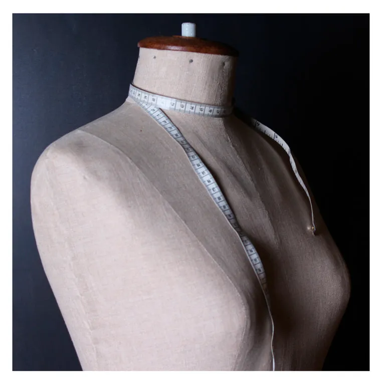 A dress form with a measuring tape on a dark background